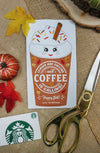 A festive fall-themed flat lay featuring a printed card with a cute, smiling coffee cup illustration topped with whipped cream, sprinkles, and a cinnamon stick. The cup has the message 'Leaves are falling and coffee is calling! Happy fall! Love, The McKowns.' The card is placed on a burlap surface, surrounded by autumn decor, including a small pumpkin, red and yellow fabric leaves, a Starbucks gift card, and a pair of gold-colored scissors.